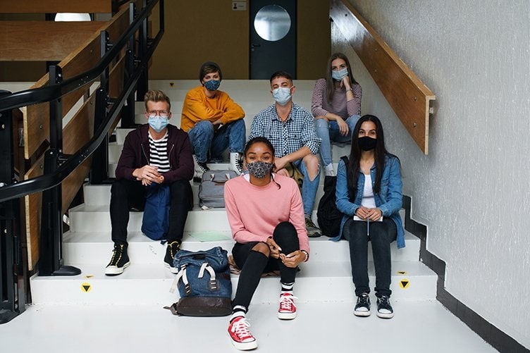 Building upon our educational roots to foster success in our community_diverse group of students sitting on stairs at school while wearing masks