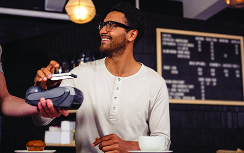 Man in glasses hovering phone over payment terminal smiling as he makes a purchase