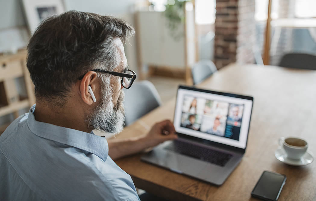 Mature man at home watching webinar in front of laptop with coffee.