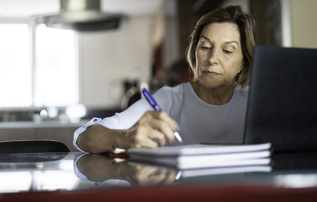 Mature woman writing on a notepad in front of her computer while attending a webinar