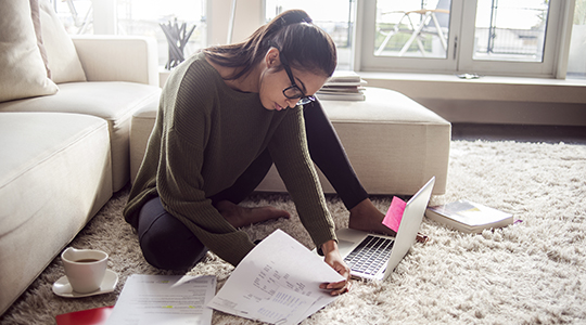 young woman reviewing finances in her living room with laptop and papers