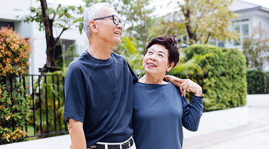 Happy retired senior Asian couple walking and looking at each other with romance in outdoor park and house in background
