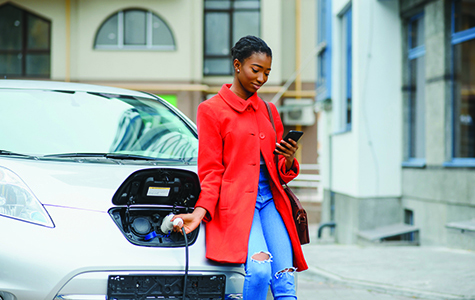 Young woman in bright red coat charging electric car at the charging station.