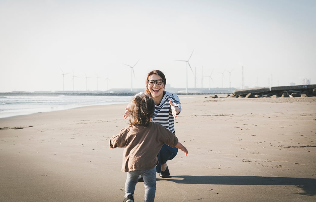 Mother and child playing in the beach where there is wind power station in the background.