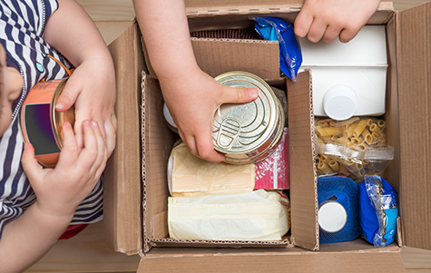 Children opening a food delivery box at home, online ordering. Grocery store delivery. Box full of food in concept donation boxparcel. Delivery during quarantine due to coronavirus COVID-19 disease