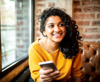 Woman smiling looking at someone off camera while holding her mobile phone.