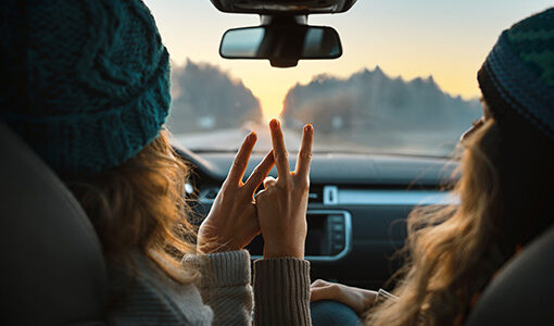 View from back seat of two women in front seat of car holding up peace sign