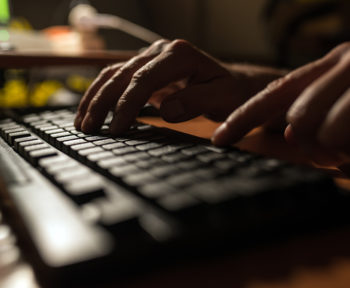 Fingers pressing on a computer keyboard in the dark .