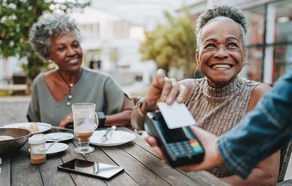 Two older ladies using tap to pay with credit card at lunch onpoint credit education month 2025
