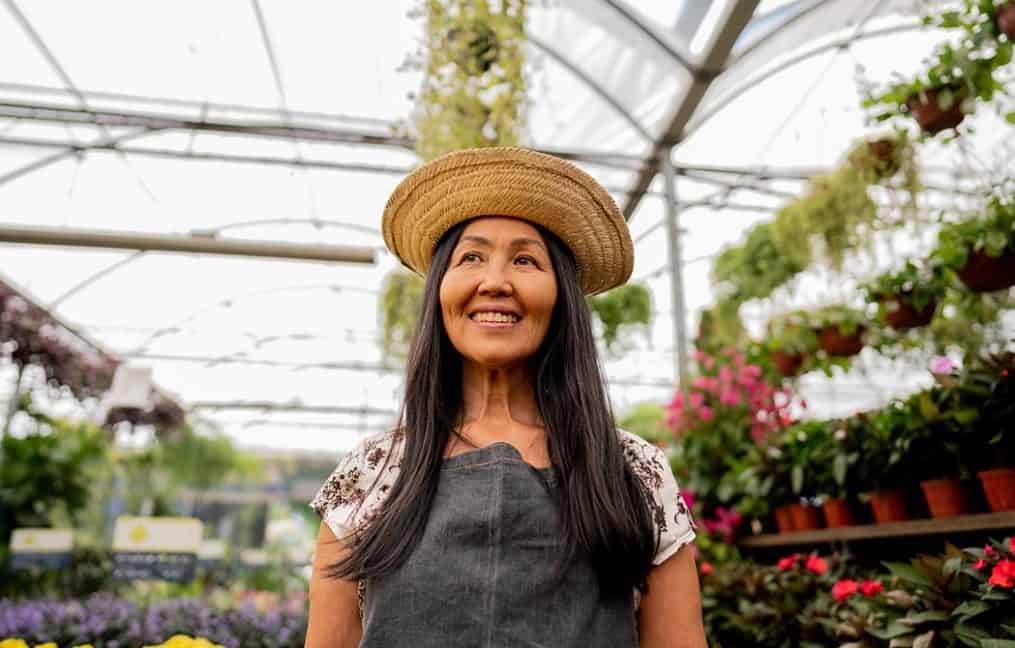 Woman in greenhouse with flowers wearing straw sun hat smiling onpoint small business campaign 2025