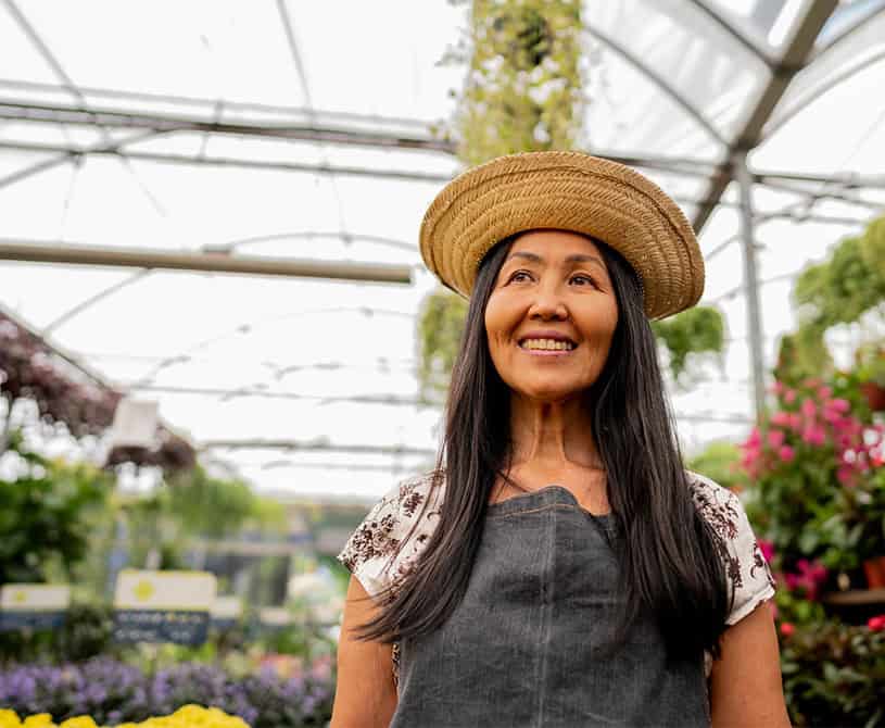 Woman in greenhouse with flowers wearing straw sun hat smiling onpoint small business campaign 2025 home page