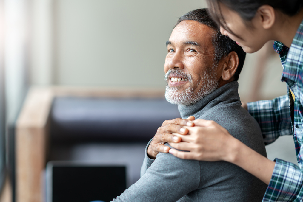 Smiling happy older asian father touching daughter's hand on shoulder looking and talking together with love and care