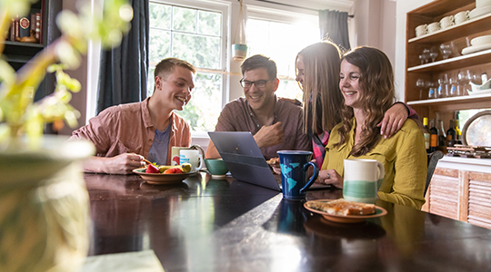 Family sitting around the dining room table looking at a laptop_540x300