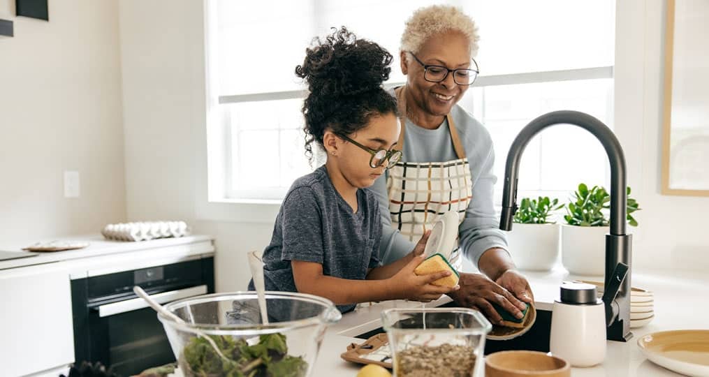 A happy grandmother and grand daughter washing dishes.
