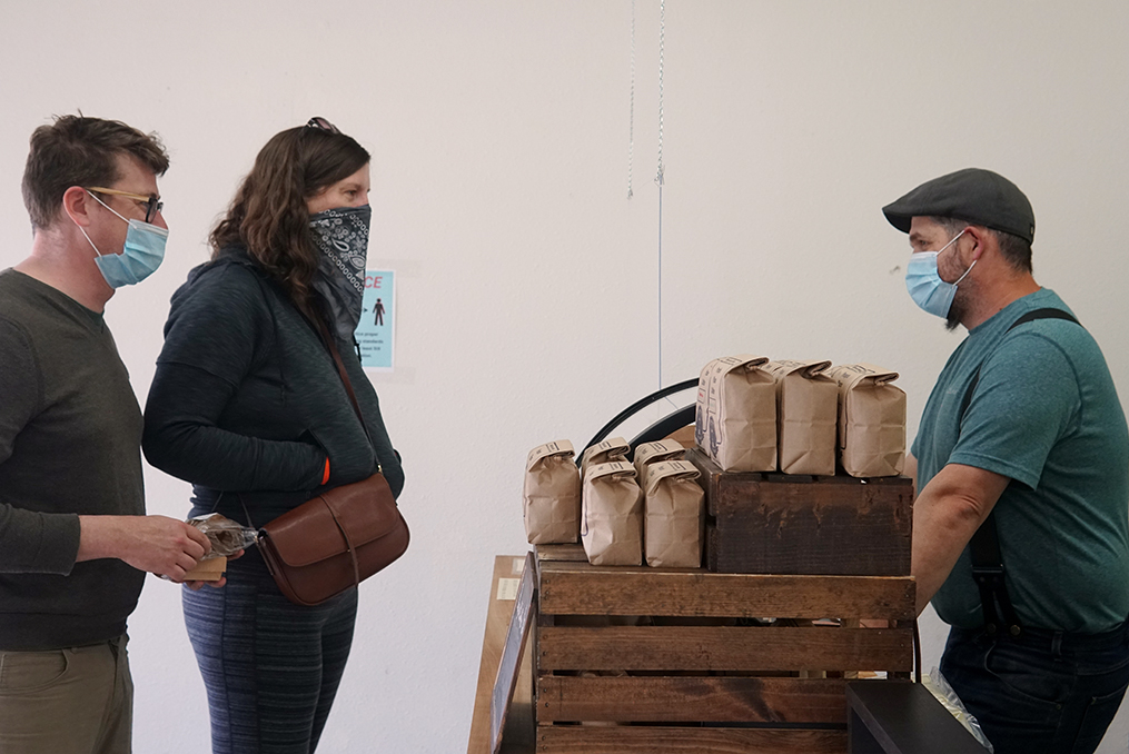 Rocky Butte Business Spotlight_Bryan serving coffee wearing mask behind safety shield