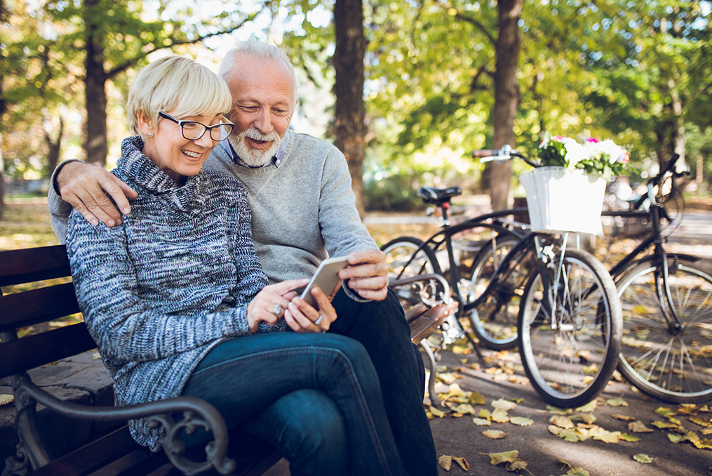 Senior Couple sitting on a park bench looking at their phone