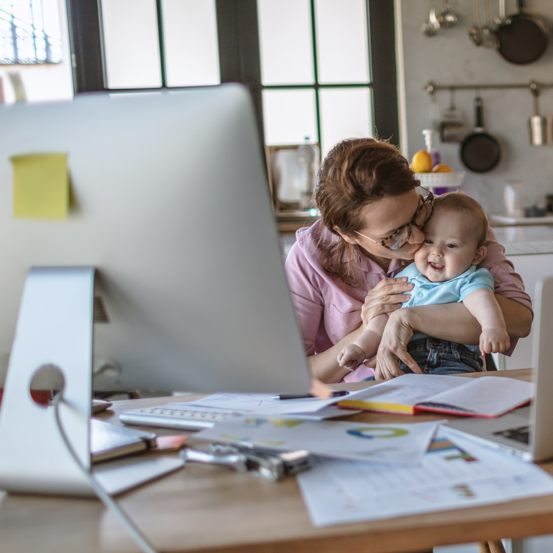 mom kissing baby while sitting at the dining table doing finances