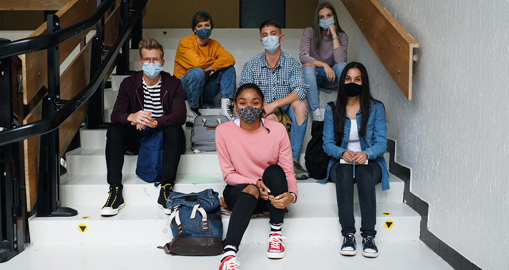 Building upon our educational roots to foster success in our community-diverse group of students sitting on stairs at school while wearing masks