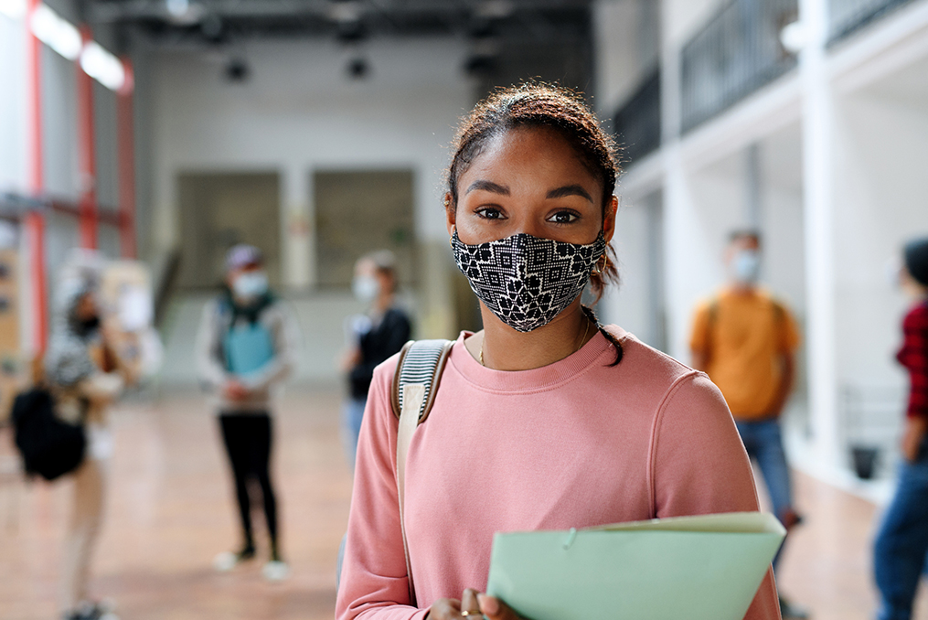 Building upon our educational roots to foster success in our community-teenage student standing in high school foyer with other students walking in background