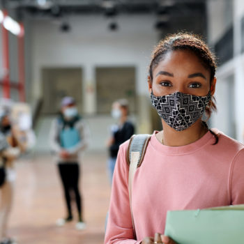Building upon our educational roots to foster success in our community_teenage student standing in high school foyer with other students walking in background