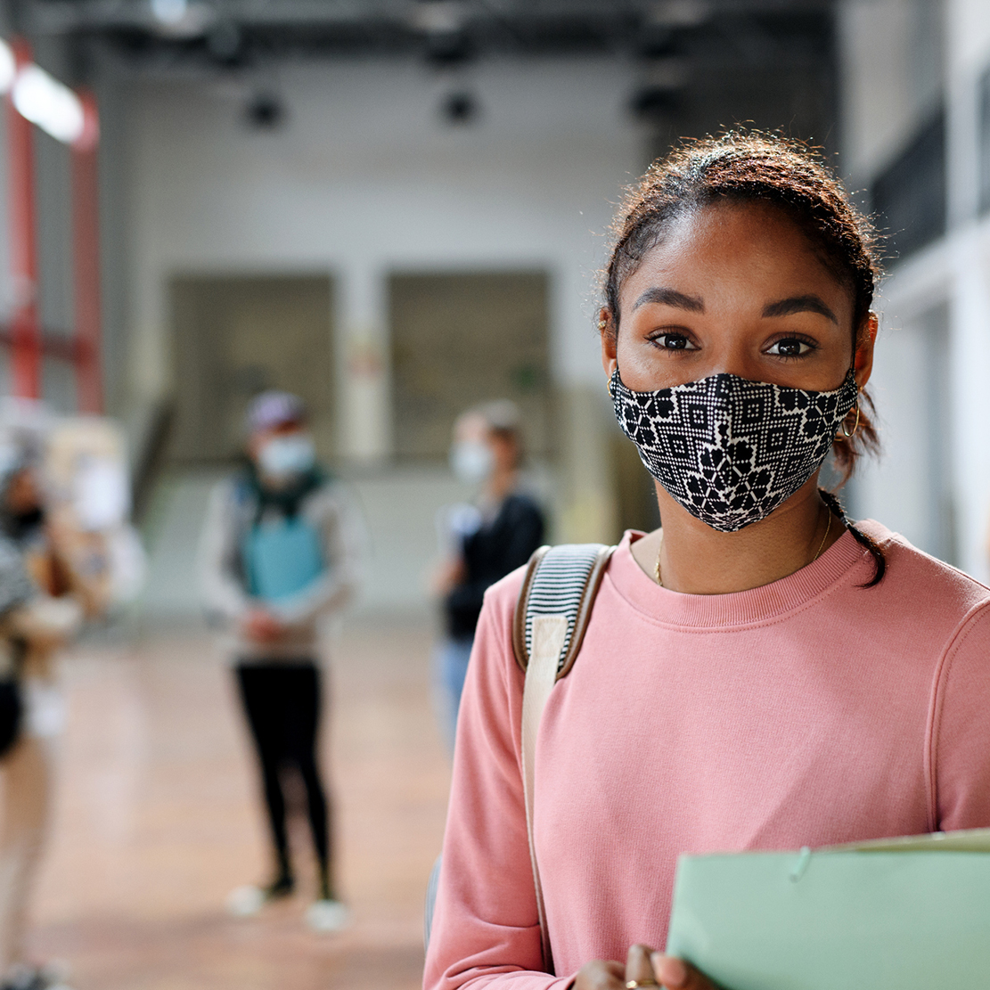 Building upon our educational roots to foster success in our community_teenage student standing in high school foyer with other students walking in background