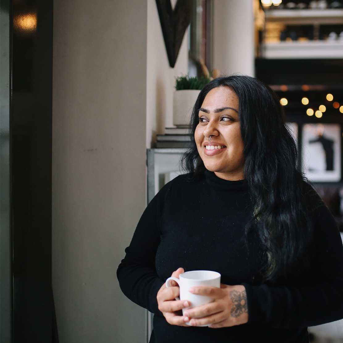 Commit to Getting Financially Fit in 2020_young woman standing in her apartment with a cup of coffee thinking about the future
