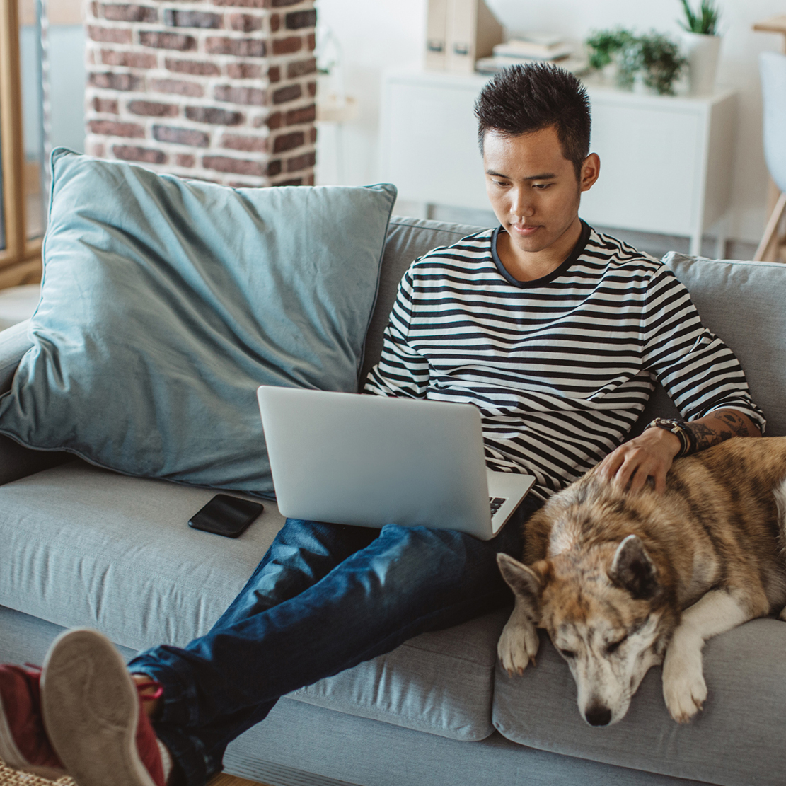 Financial Planning Resources for Home-Bound College Students_young man sitting on his couch with his dog looking at his laptop