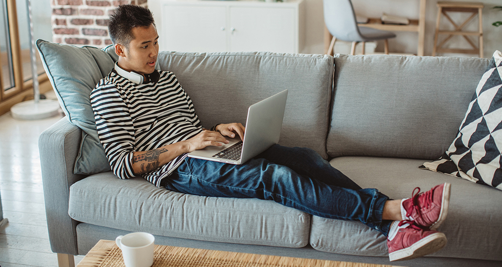 Financial Planning Resources for Home-Bound College Students_young man sitting on his couch with his laptop