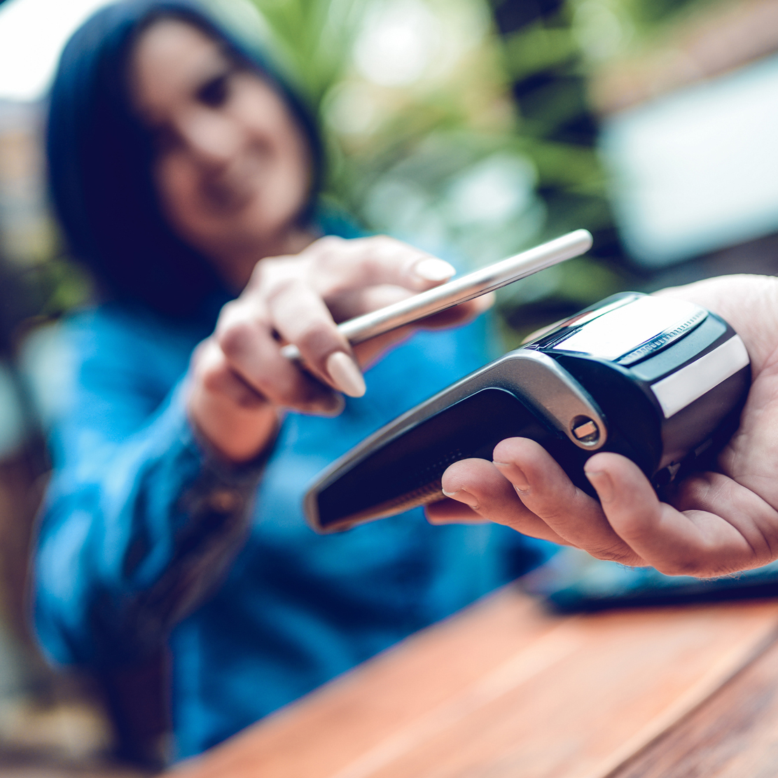 Young woman making a payment to a small business with her connected cell phone
