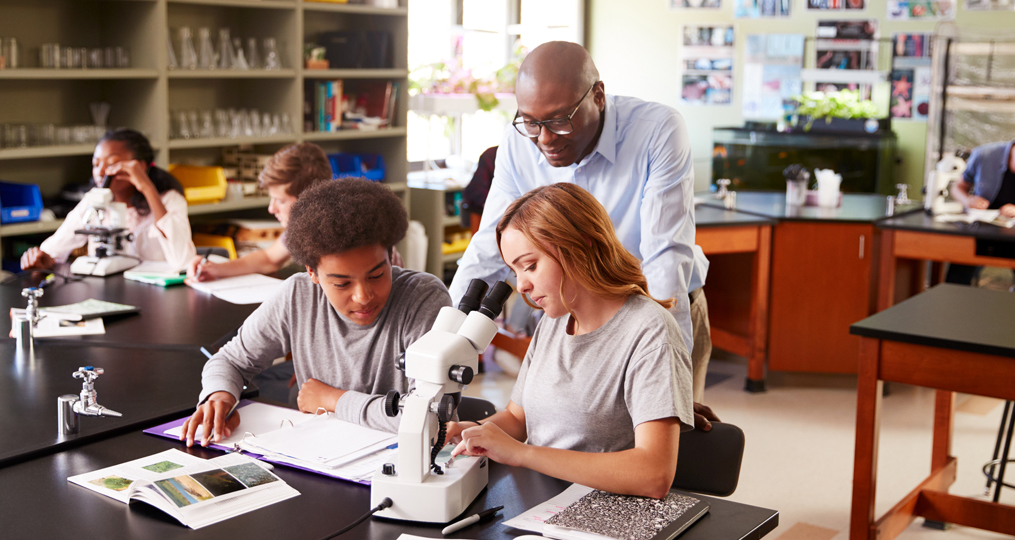 OnPoint Celebrates 2019 National Teacher Day_science teacher helping two students work on a lab project in the classroom