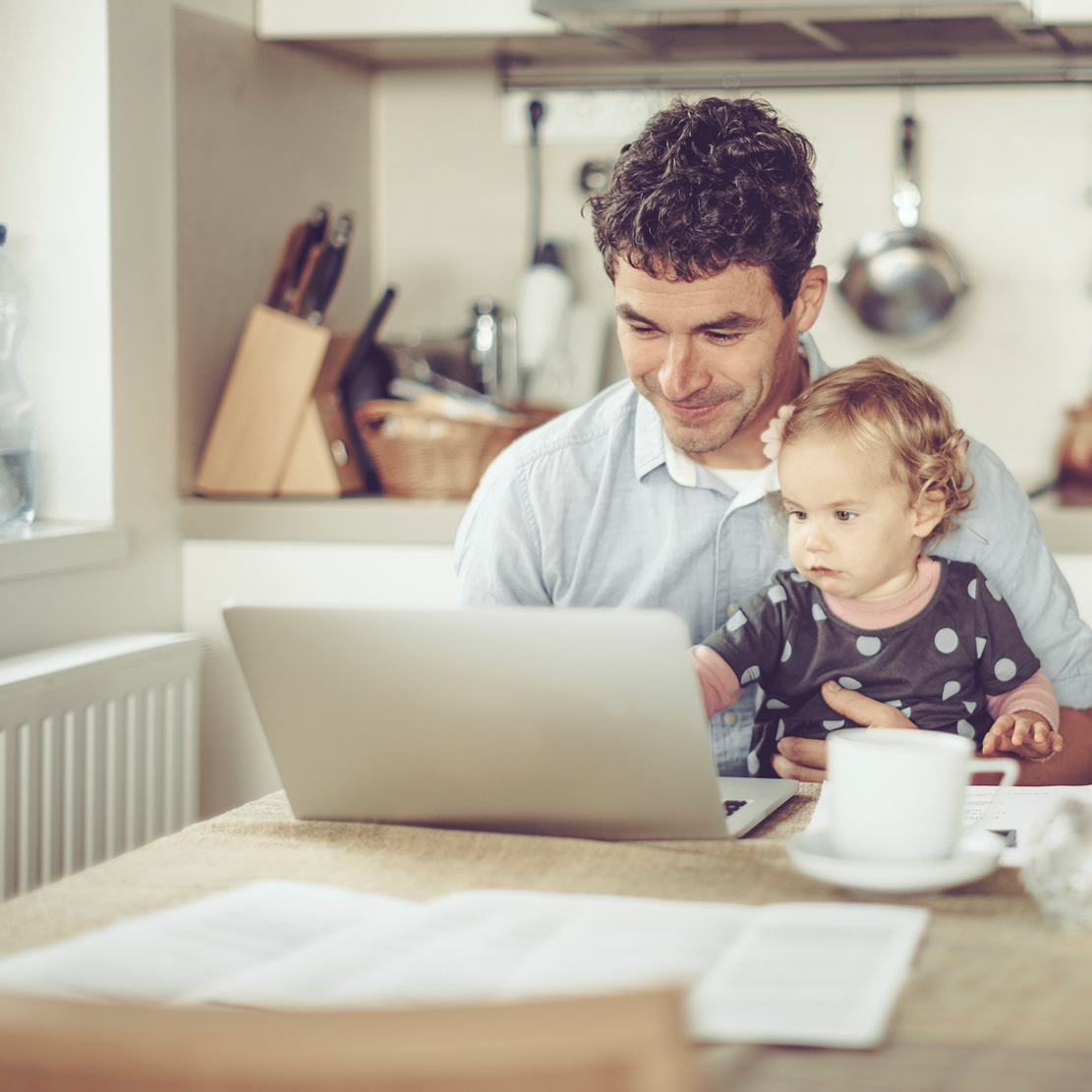 Strategies for Quitting the Paycheck-To-Paycheck Life_Father and child sitting at the kitchen table looking at laptop