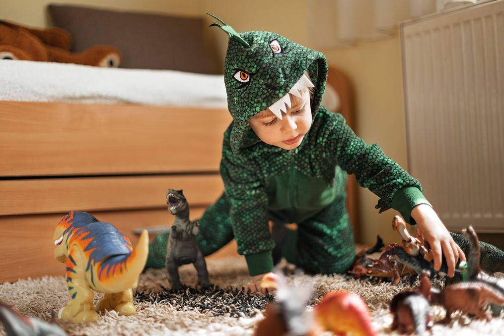 CUNA Youth Savings Month 2021_young boy in dinosaur costume playing with toys in his bedroom