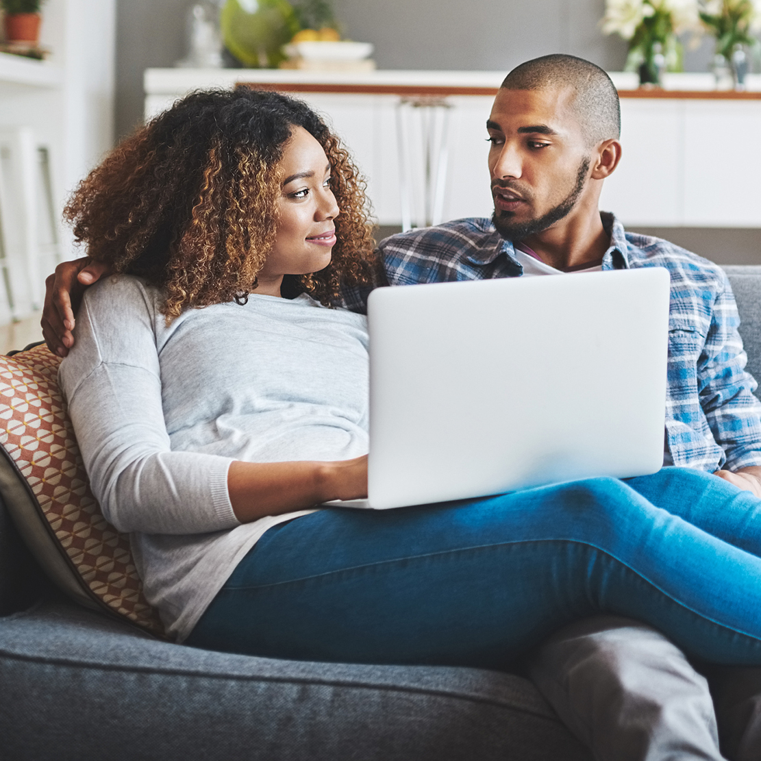 couple sitting on their couch with their laptop looking at one another
