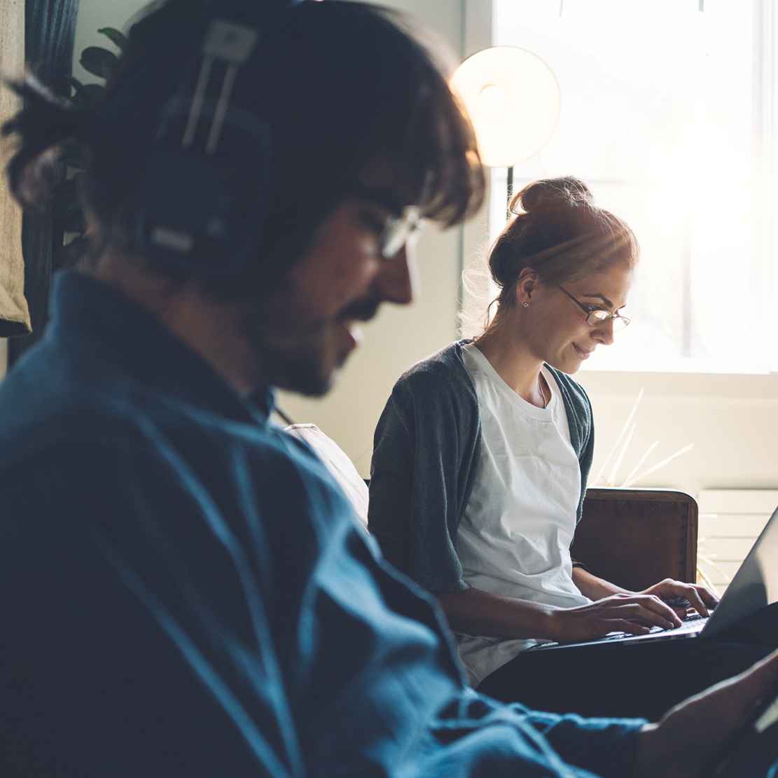 Open Multiple Savings Accounts_couple sitting together on their couch she's looking at her laptop and he is listening to music