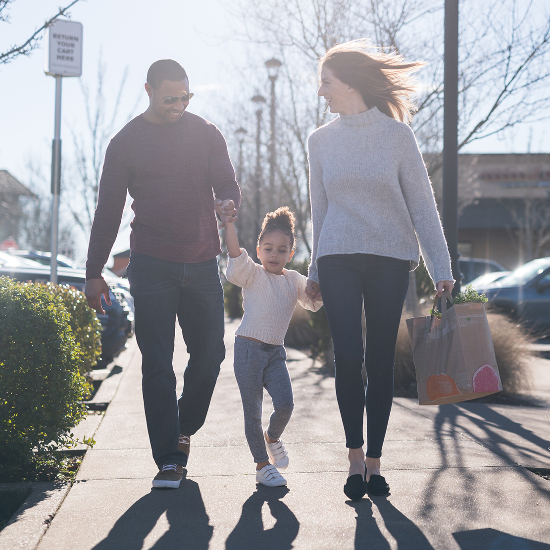 family walking through the parking lot carrying grocery bags
