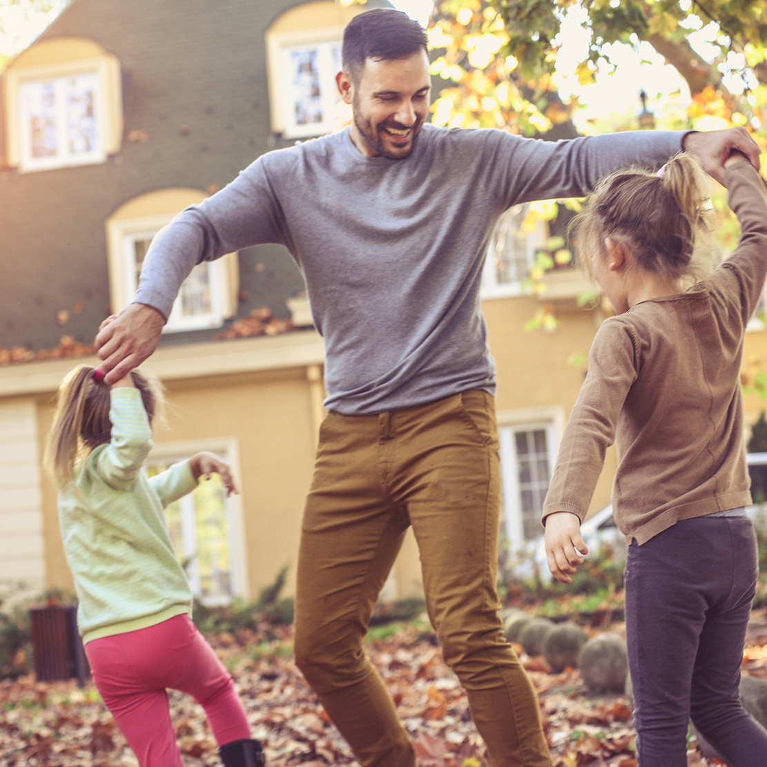 father dancing and playing with his two daughters in their yard among the fall leaves