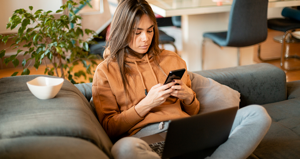 why malware is dangerous and how to protect yourself_woman sitting on coach reviewing looking up malware solutions on her mobile phone