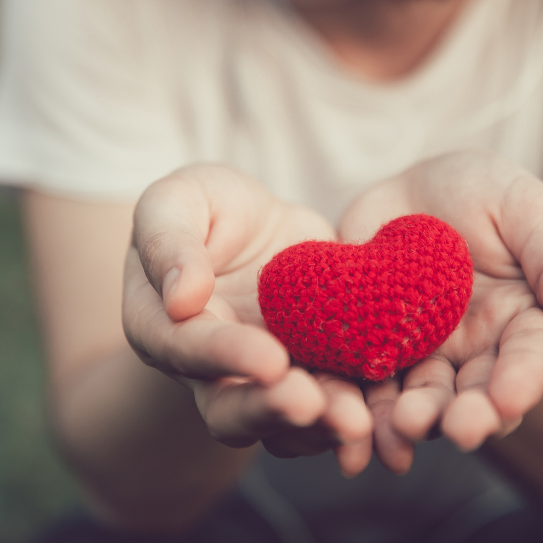 young girl holding a heart made of yarn in the palms of her hands