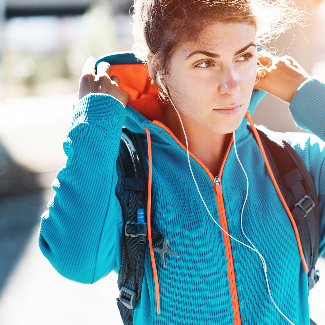 young woman listening to music on her headphones while putting on her hood