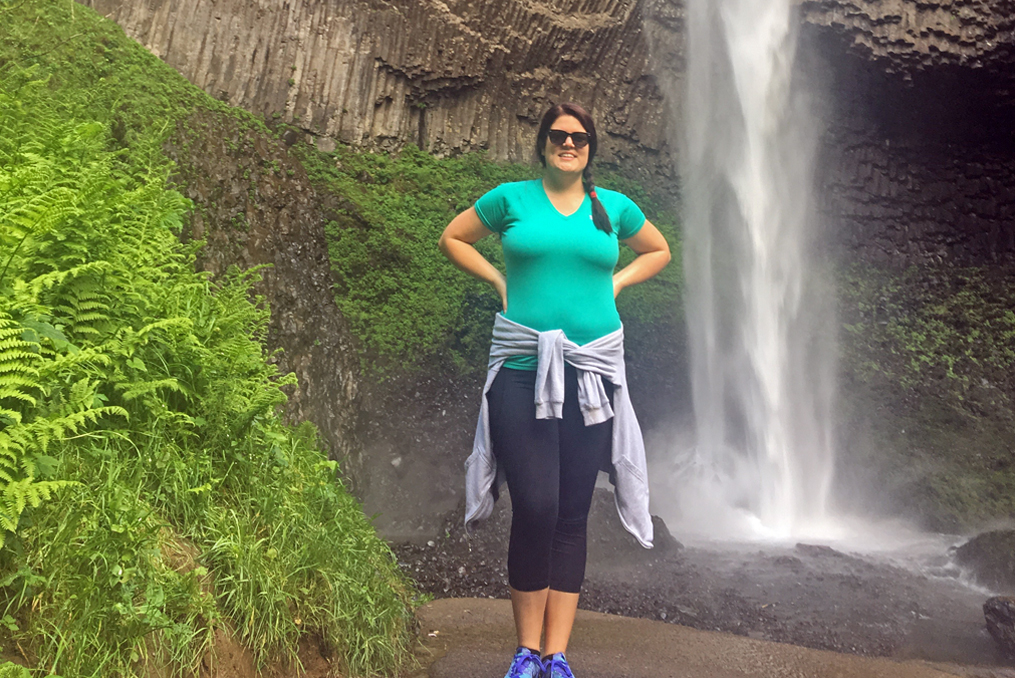 Lucy standing at the base of a waterfall while on a hike