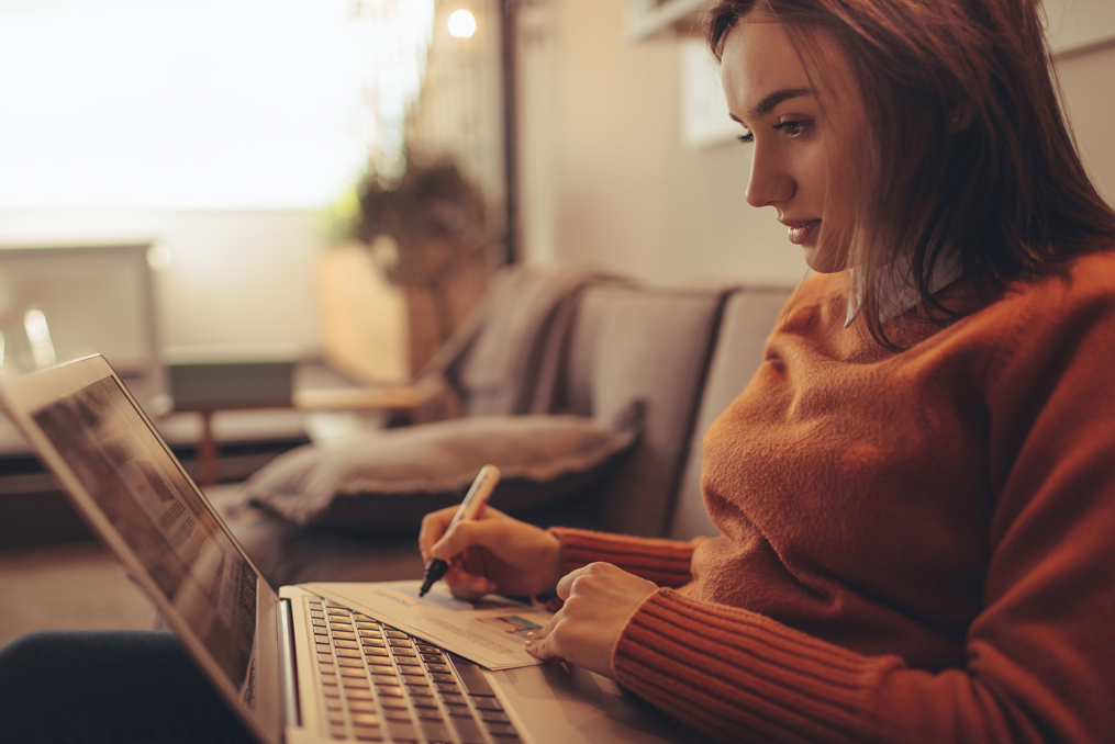 Young woman sitting on her couch with her laptop using a worksheet