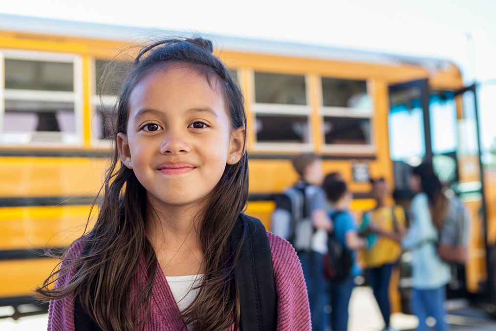 How to Get the Most From Your 529 Plan_young girl smiling standing next to the school bus with other children in the background