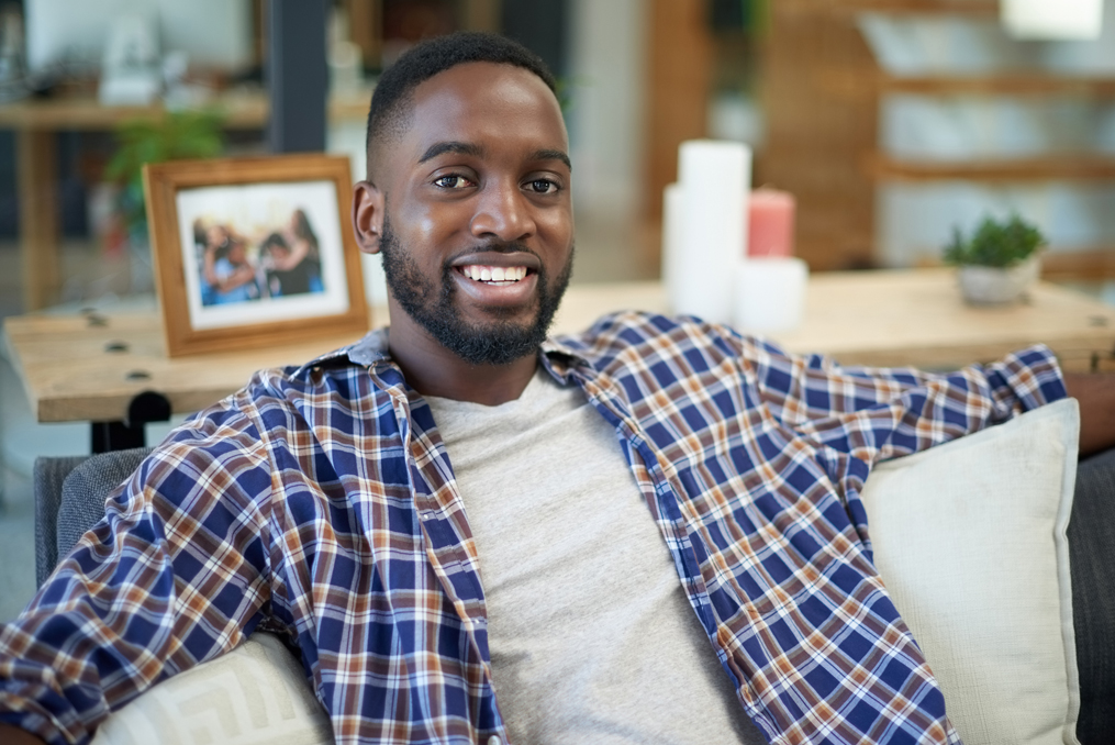Managing Student Loan Debt during COVID-19_Happy young man sitting on the couch in his home