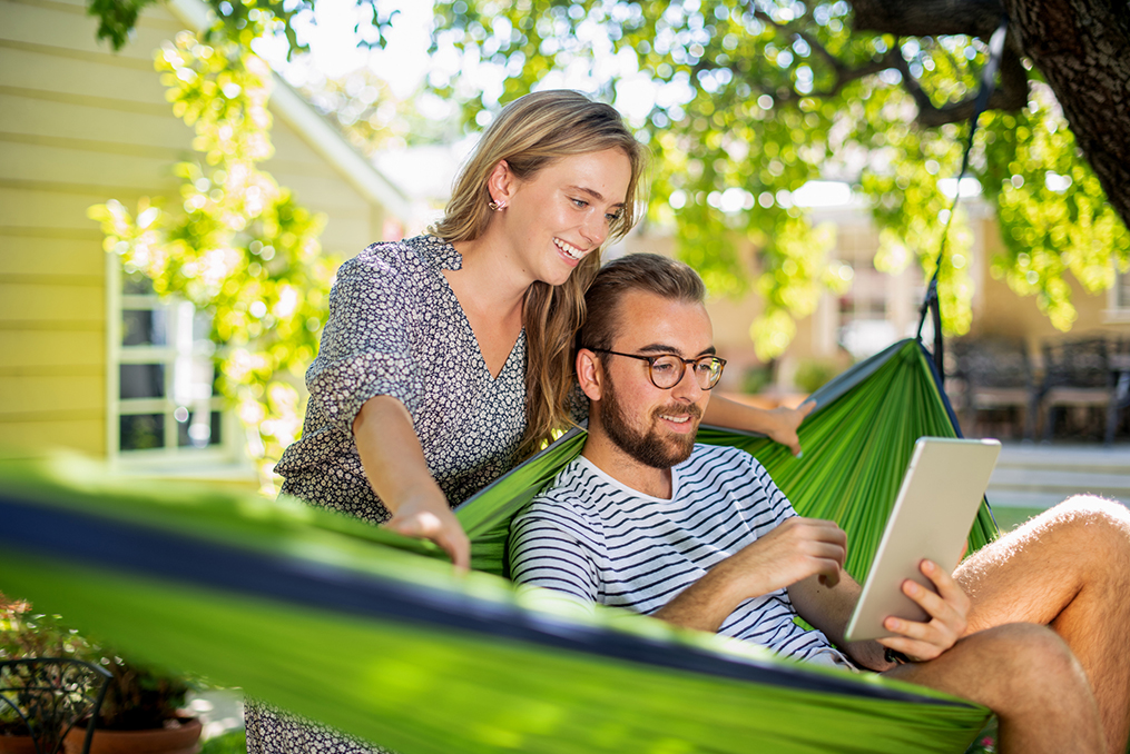 Take the time to organize your finances_Young man and woman sitting in a hammock reviewing personal finances