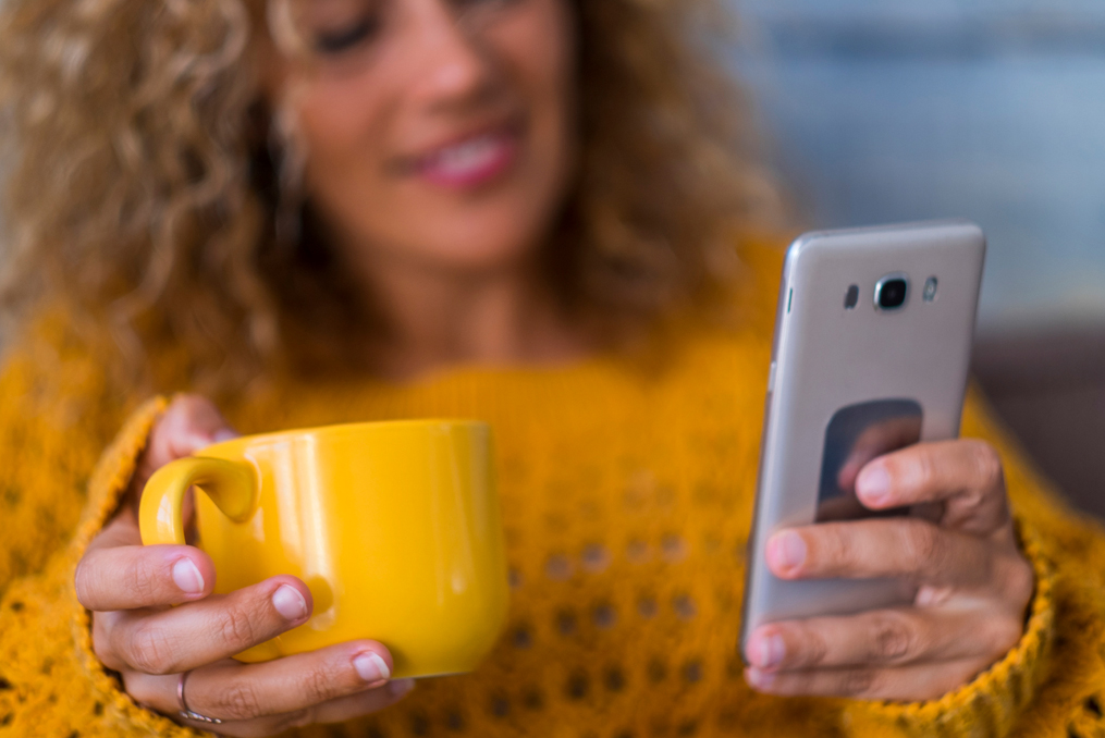 Save for Retirement When You Have Debt_woman using her phone while drinking a cup of coffee