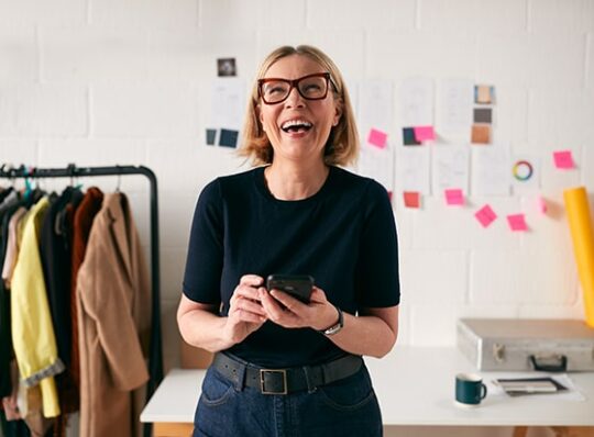 Business checking landing page-woman managing her business checking account using her mobile phone
