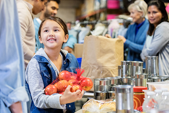 Young girl helps at food bank holding bag of oranges