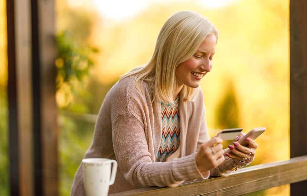 woman using debit card on phone on porch smiling