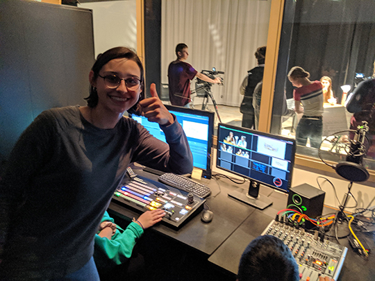 Students in the production room editing film and giving a thumbs up to the camera