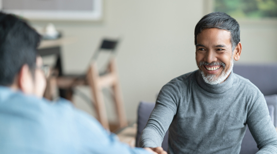 Confident mature Asian man sitting, smiling and shaking hand